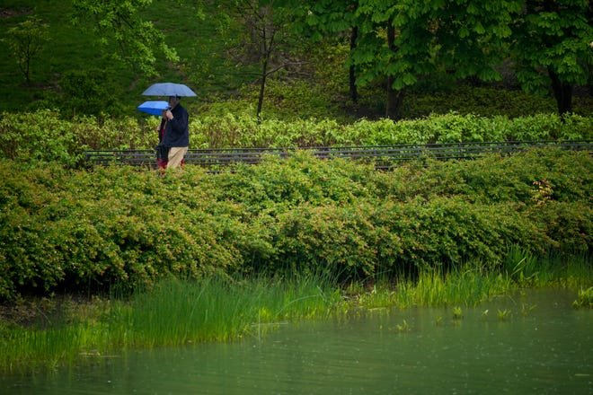 People with umbrellas walk past Mirror Lake on May 7, 2023, the date of Ohio State University’s Spring Commencement. The school said it remains committed toward building a more sustainable campus even as it has fallen short toward some of its goals.
